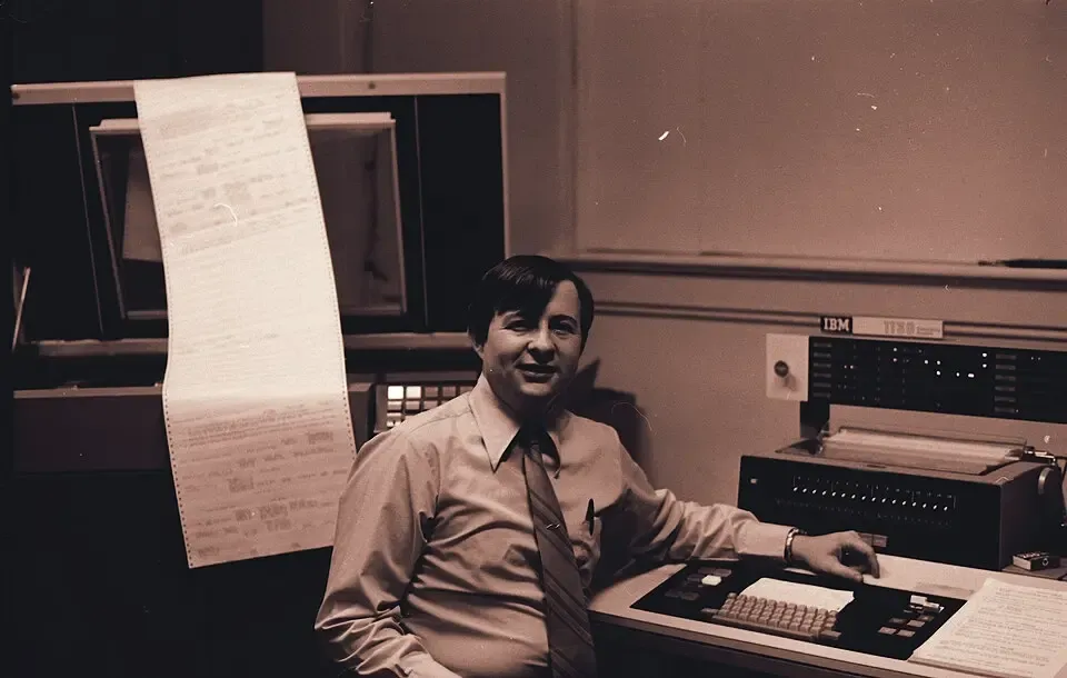 A programmer at an IBM 1130 with a long fanfold printout